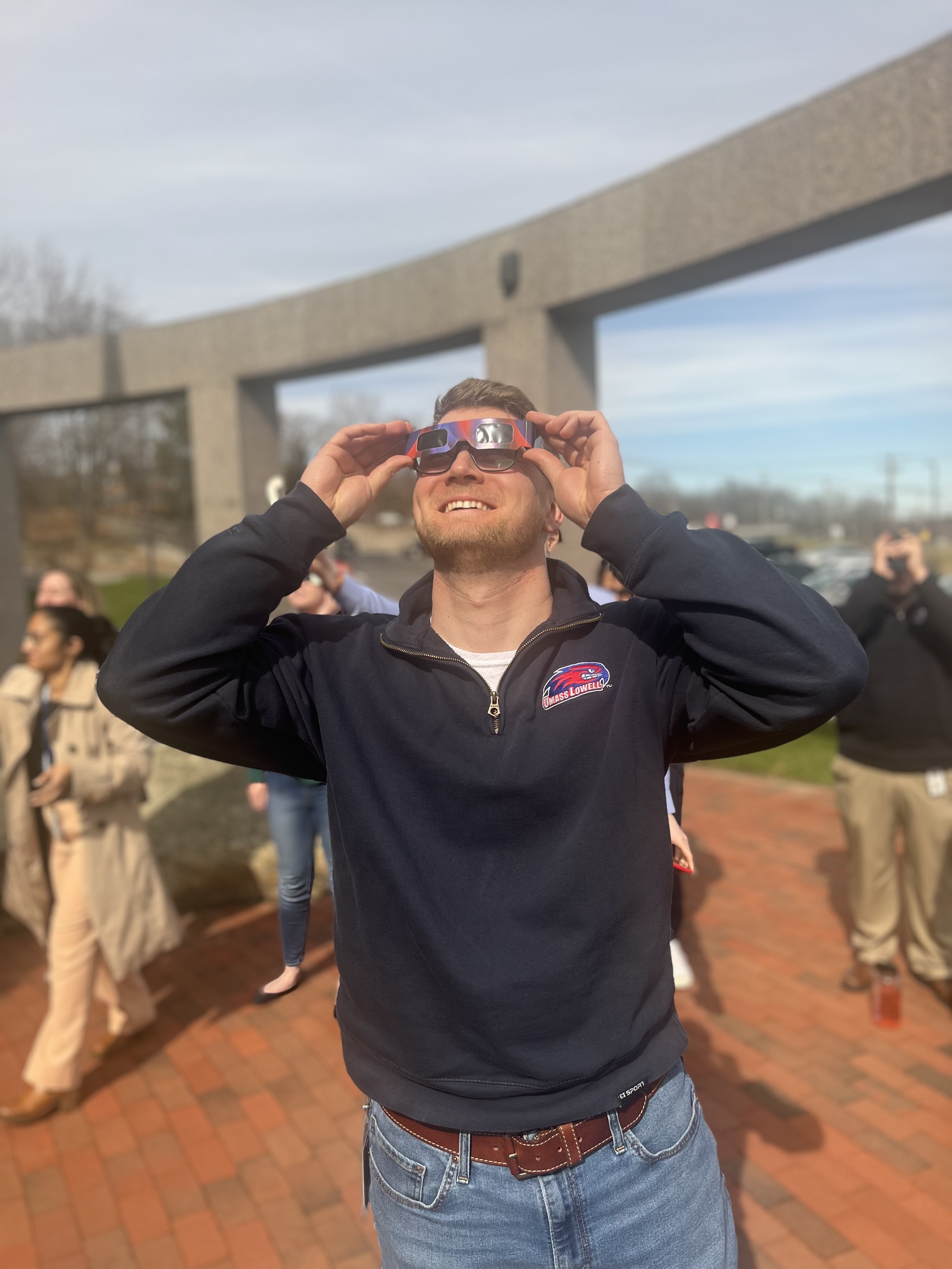 white male in blue pullover smiles while looking up wearing solar eclipse glasses