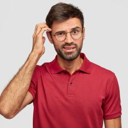 young man in a red shirt with puzzled expression scratches his head