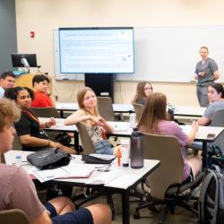 Early college students are sitting at their desks and look excited.