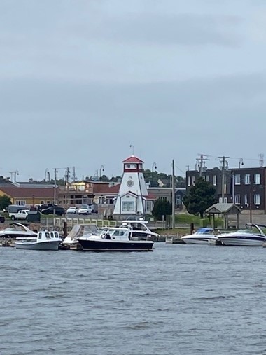 A lighthouse sits on the shore with boats floating in the ocean water in front of it on an overcast day.