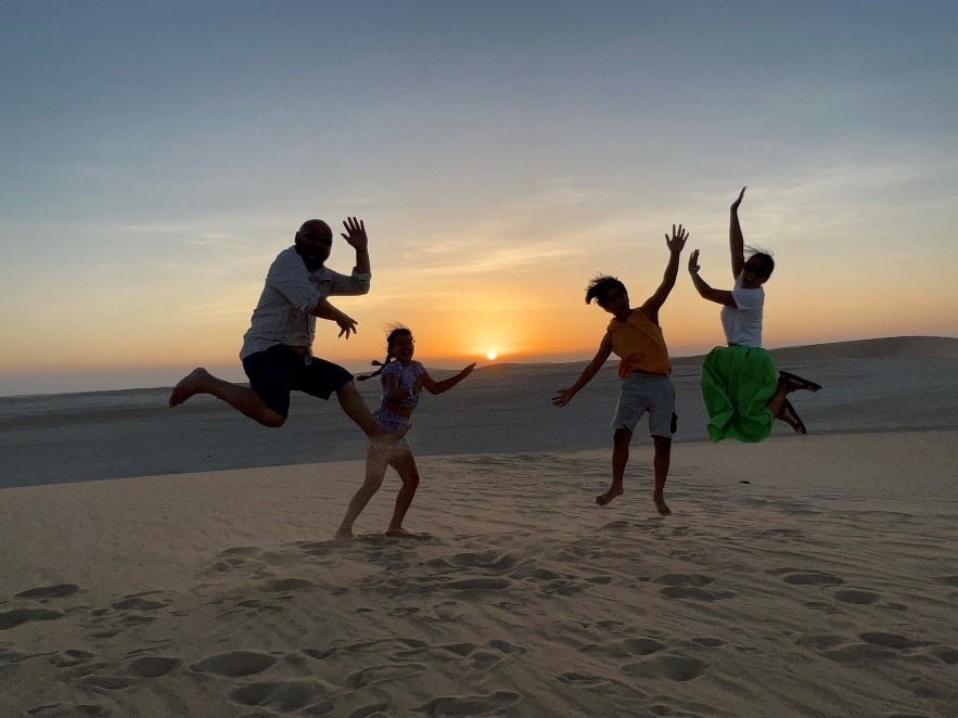 4 silhouetted people jumping on beach with the sun setting behind them.