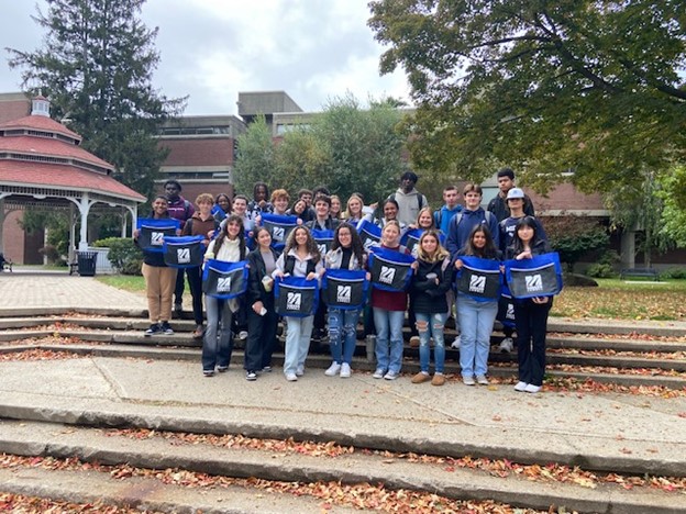 Mixture of students pose with UML labeled bags on steps