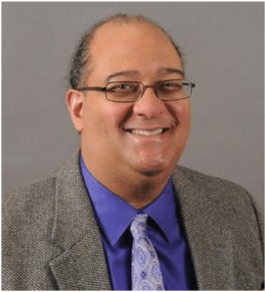 a light brown skinned man smiling and wearing glasses dressed in professional attire