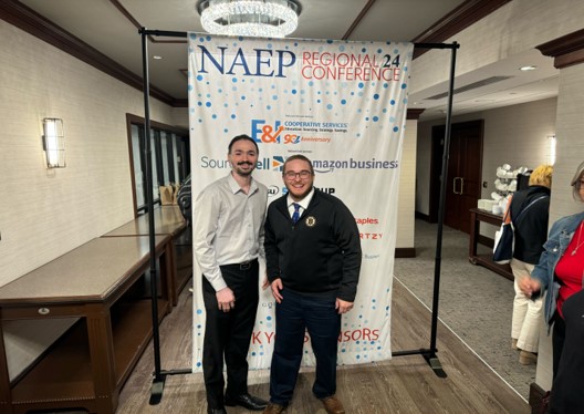 Akshit and Garret from UPST posing in front of a regional conference poster
