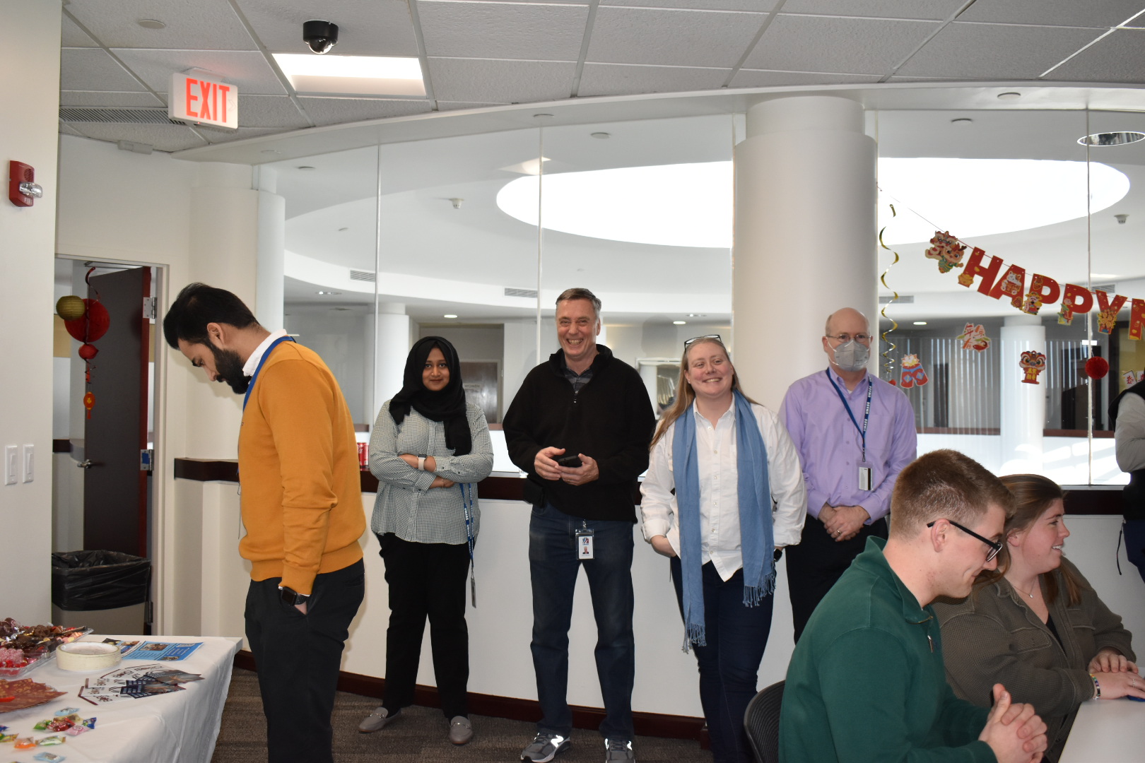 Employees stand in the University room, mingling. 