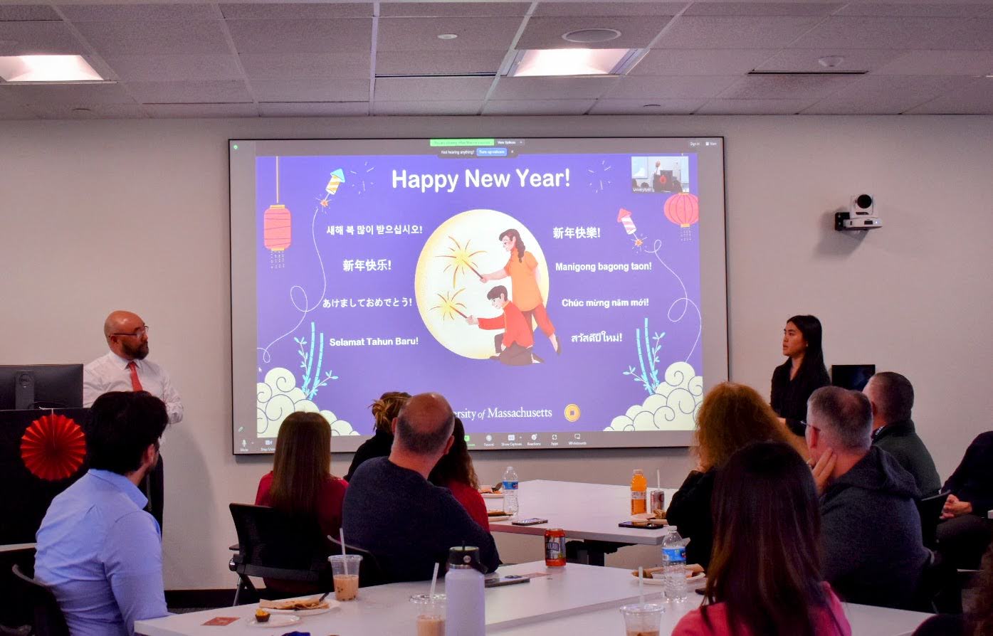 David Cho presents at a podium with a presenatation up on the screen that says, "Happy New Year," and has Happy New Year in various languages.