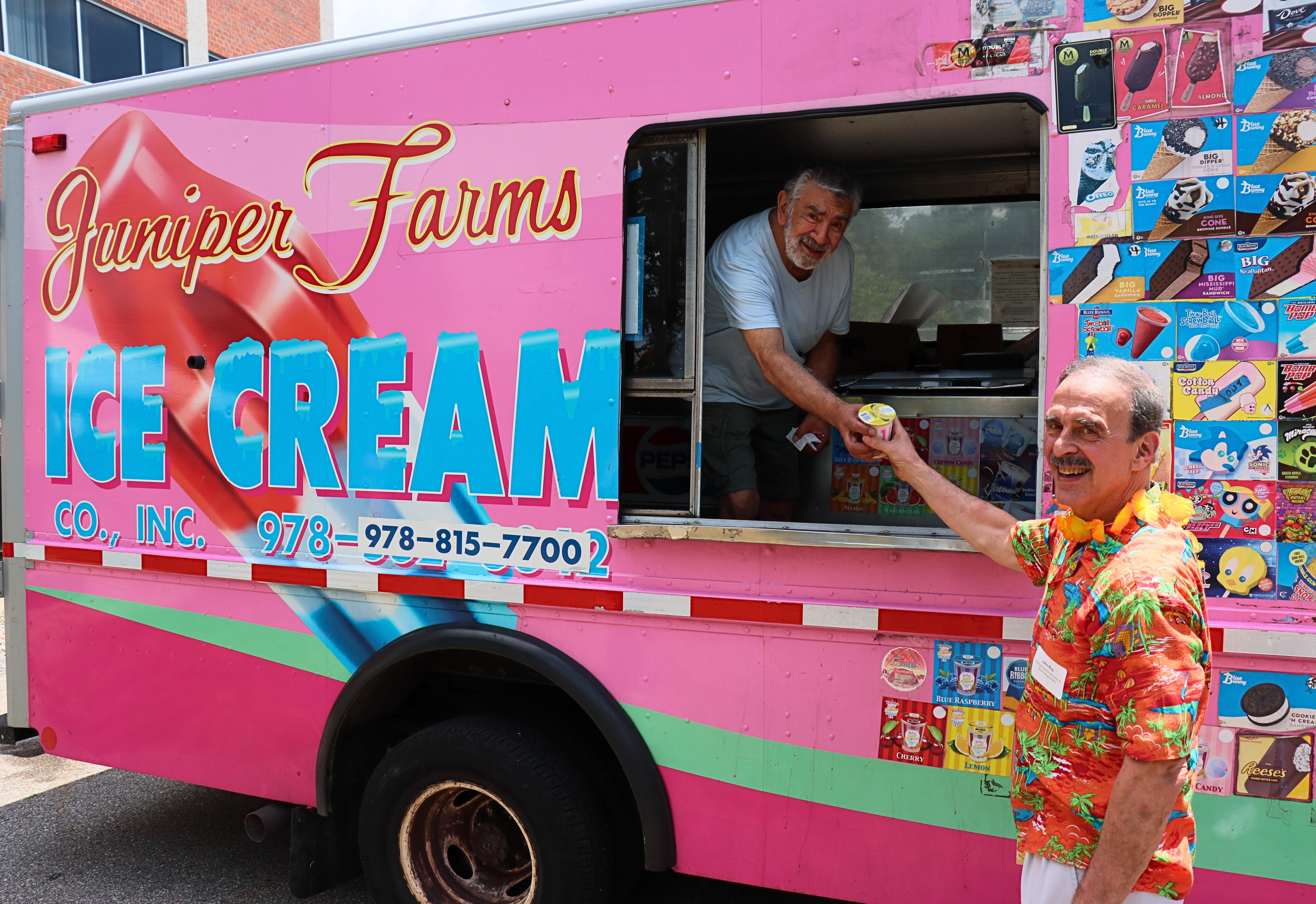 smiling man in orange hawaiian shirt holds an italian ice from a smiling ice cream truck man that is bright pink