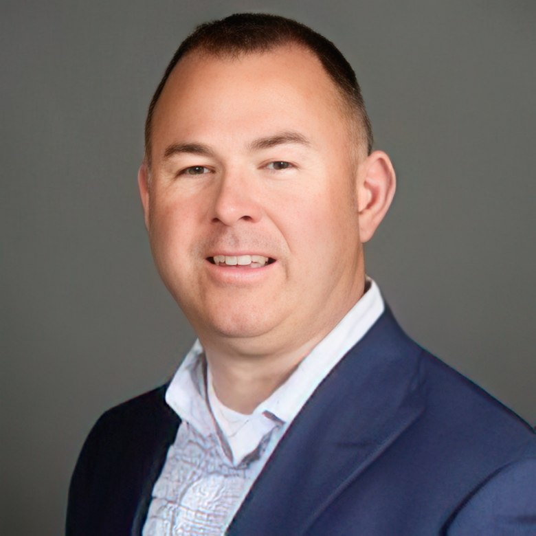 white male smiles in a headshot with navy blue blazer and light blue undershirt.