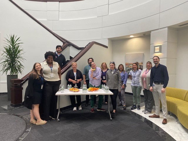group of people posing in front of a table of fruit and water.