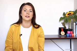 A light-skinned woman with dark hair sits with a table behind her. The table has a sunflower on it and a medal from the Paralympics.