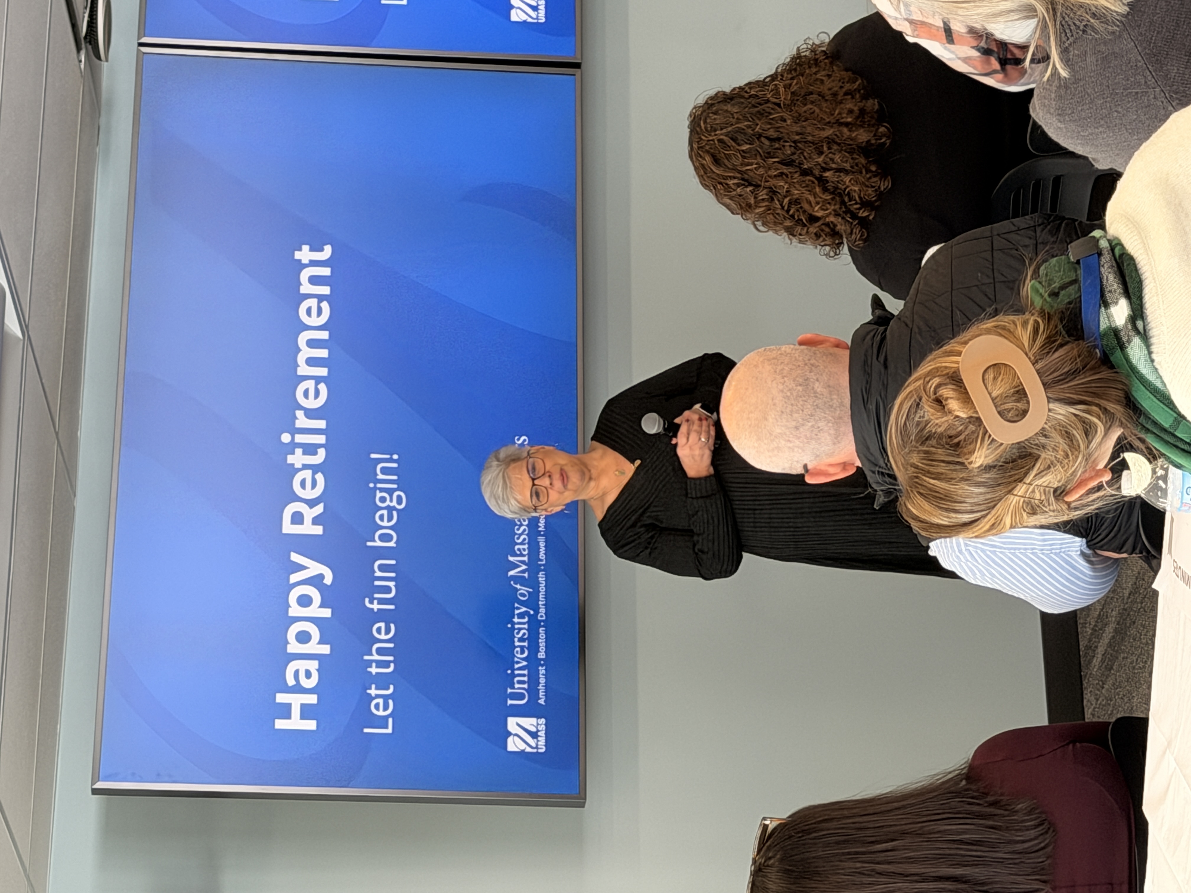 Carol Dugard standing in front of a blue monitor that says Happy Retirement