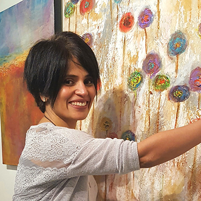 Chaya stands in front of one of her abstract art pieces smiling.