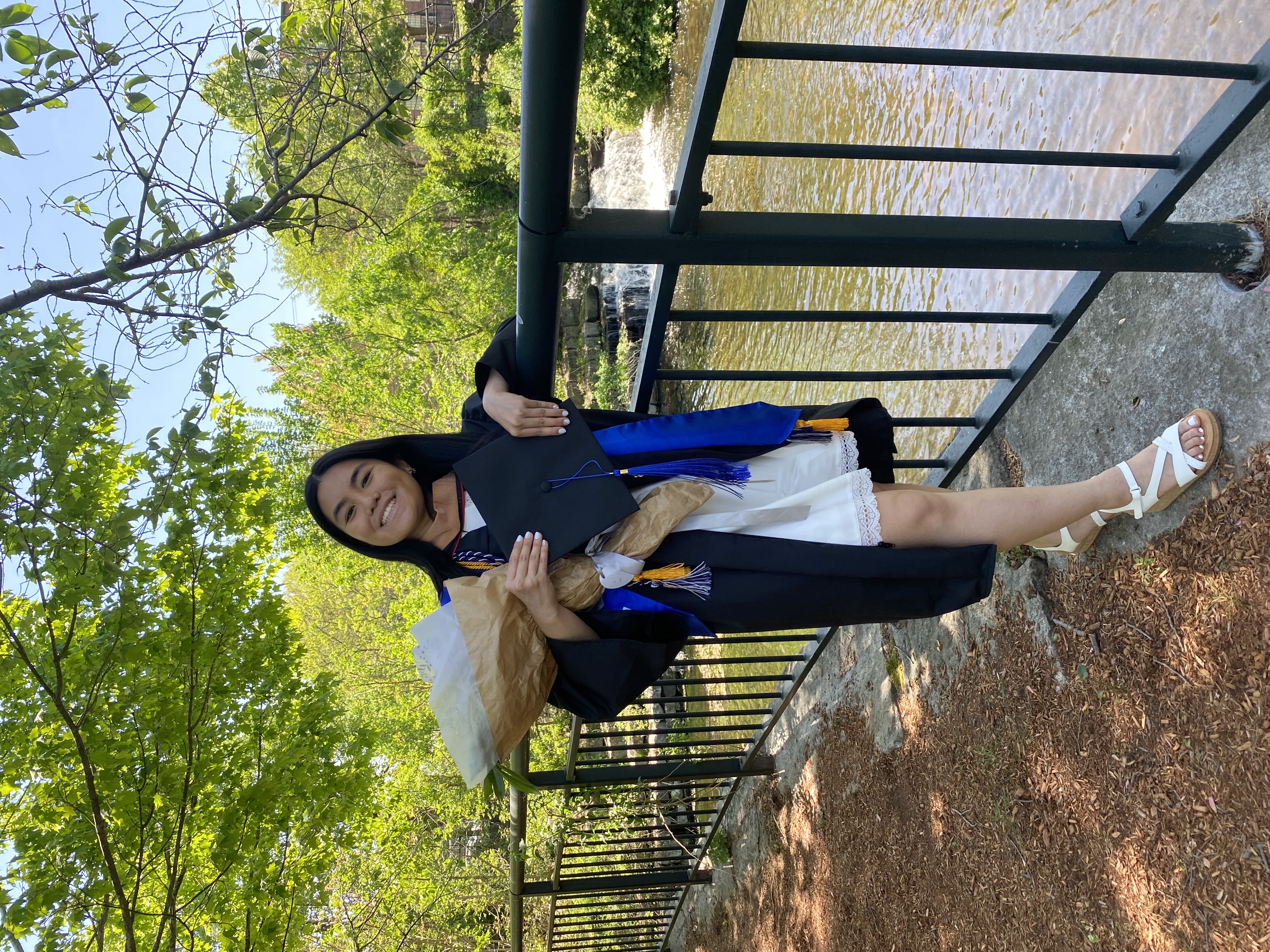 Female smiling wearing graduation gown, holding flowers and cap
