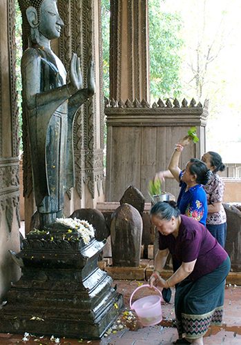 Three women sprinkle water on a Buddha statue.