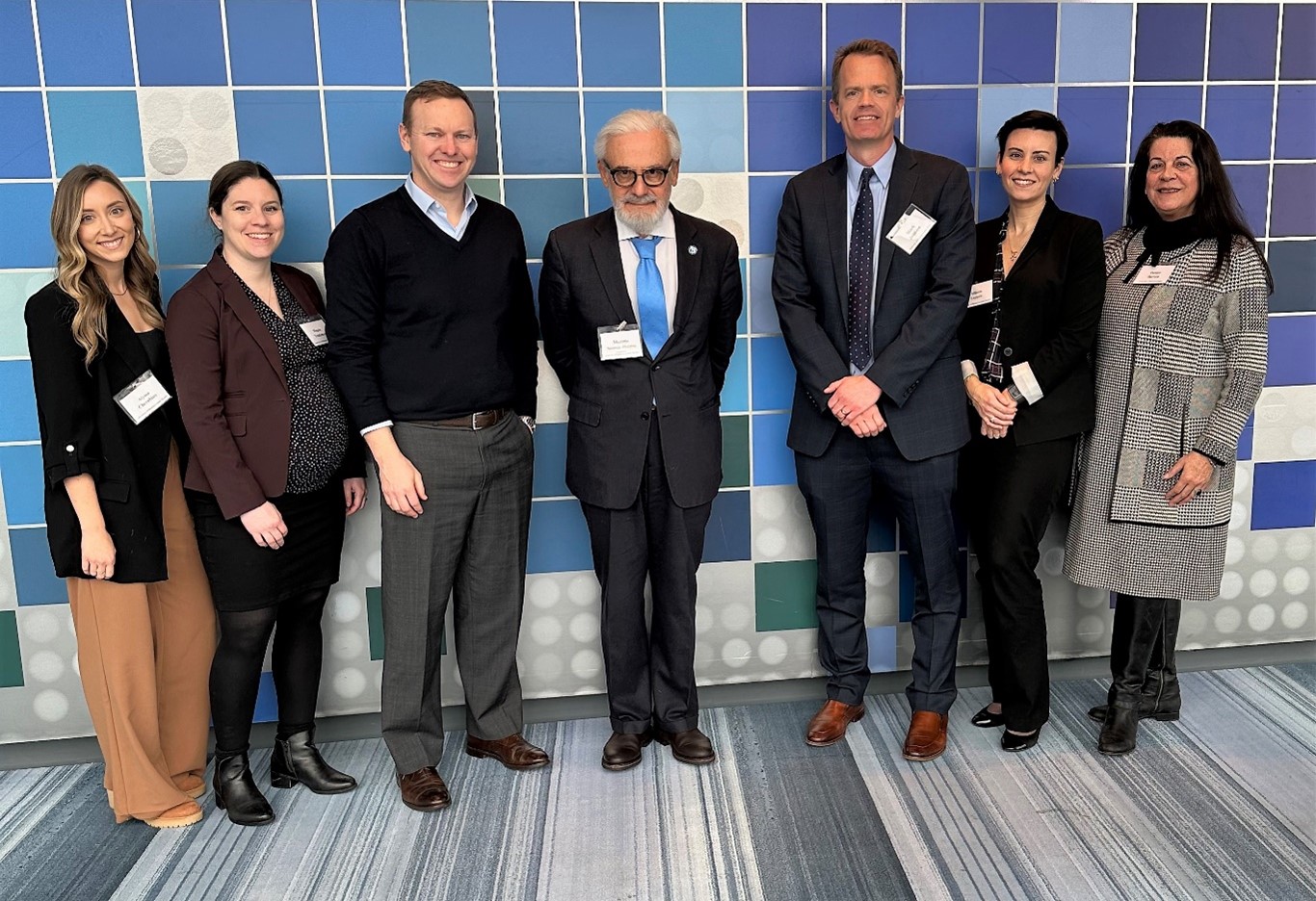 Four women, three men pose together with a background in various blue hues.