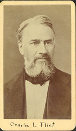 A light-skinned man with white-gray hair and a white-gray beard stares away from the camera steadfastly. He wears a white shirt and suit coat. 