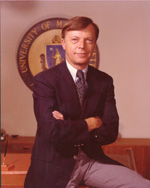 A light-skinned man with brown hair and a cleanly shaven crosses his arms and smiles into the camera.