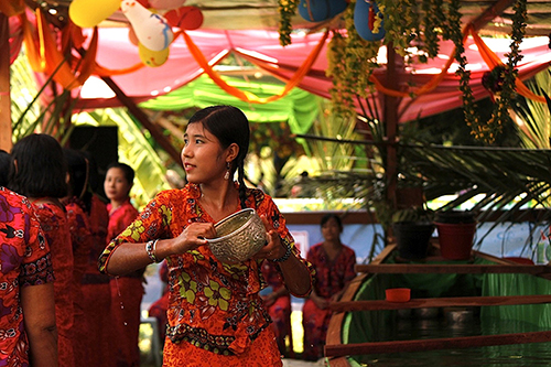 A medium-dark skinned girl in a a colorful orange and green outfit tilts a golden bowl.