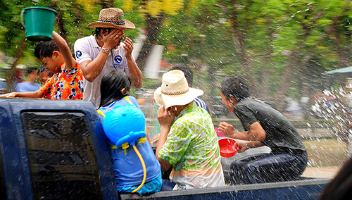 A man wipes water from his face as children shriek at water being sprayed at them.