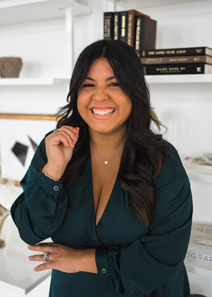 Vanessa leans against a table smiling with books behind her.