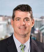 professional photo of david brunelle in a dark suit, pale blue dress shirt and a green neck tie.
