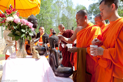 Khmer monks dressed in orange robes sprinkle water on statues of Buddha.