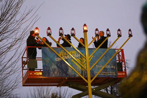 Members of the Jewish community stand on a lift and manually light the Boston Common Menorah.