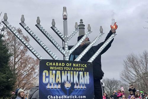 A man stands on a ladder, lighting the first candle of a large menorah.
