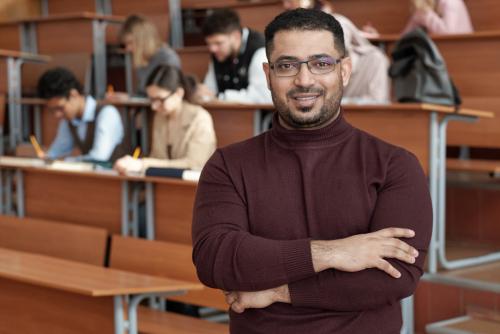 a professor standing in an auditorium with multiple students behind him doing work.