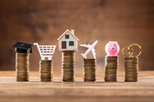 stacks of coins with various items on top of each. (from left to right: graduation cap, shopping cart, house, airplane, piggy bank, rings)