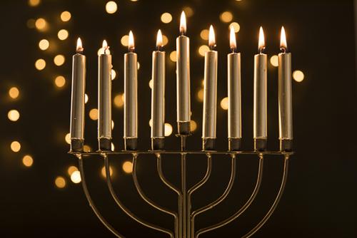 A menorah with all its candles lit and golden bokeh in the background.