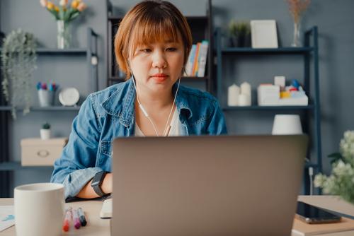 A medium-skinned woman works at a laptop in her apartment.