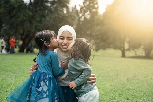 A muslim woman is kneeling as two little girls kiss her on each cheek.