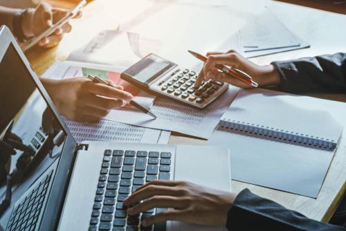 hands holding a pen using a calculator in front of a laptop