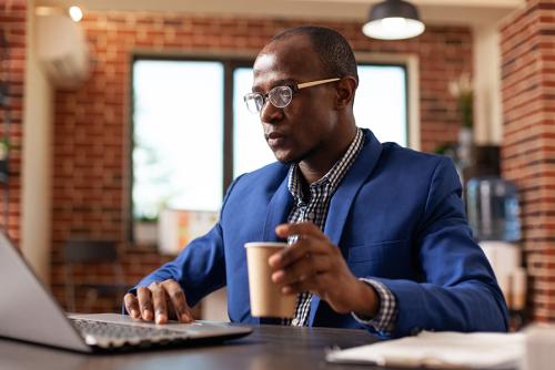 A dark skinned man sits at a computer reading.