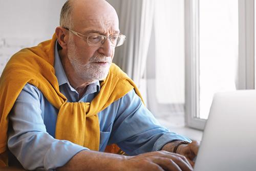 Older light-skinned man with glasses working on a laptop.