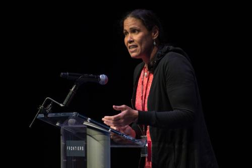 Wanda Díaz-Merced, a medium-dark skinned woman stands at a podium presenting.