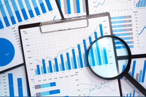 Magnifying glass on top of a piece of paper with bar charts on a clipboard
