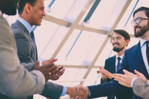 "Two darker skin men shaking hands with two fairer skinned men."