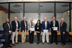 7 men and one woman standing to pose for a picture while holding certificates