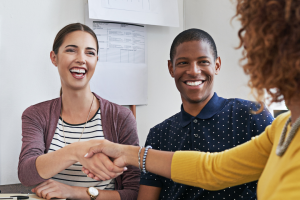 Two women, one white and one brown, shaking hands over a smiling black male