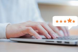 close up of a light skinned male hand typing on a laptop with a floating voice-bubble showing a four star rating
