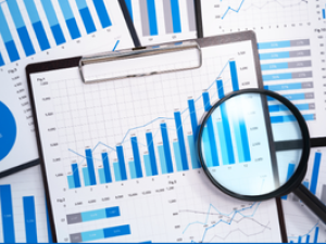 Magnifying glass on top of a piece of paper with bar charts on a clipboard