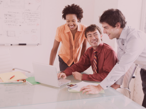 "One darker skin woman and two fair skin men looking at a laptop and smiling."