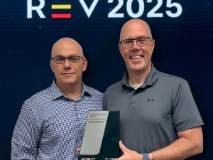 Two UMass employees standing side by side holding an award in front of a logo for company Jaggaer and a graphic logo for the REV 2025 conference