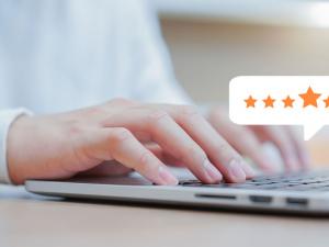 close up of a light skinned male hand typing on a laptop with a floating voice-bubble showing a four star rating