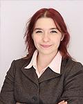 Student Trustee Ava Marino is smiling and wearing a brown tweed blazer with a pink shirt and a grayish background