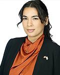 Student Trustee Gina Cuba is smiling, wearing a black blazer with an orange blouse, wearing a small cross around her neck and a flag pin on her lapel, and a white background