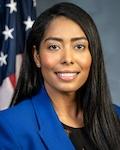 Juana Matias in a royal blue blazer and black shirt with American flag in background
