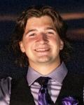 Student Trustee Travis Emerson is smiling, wearing a gray collared shirt with black vest, purple tie and purple handkerchief in chest pocket, with a dark shadow background